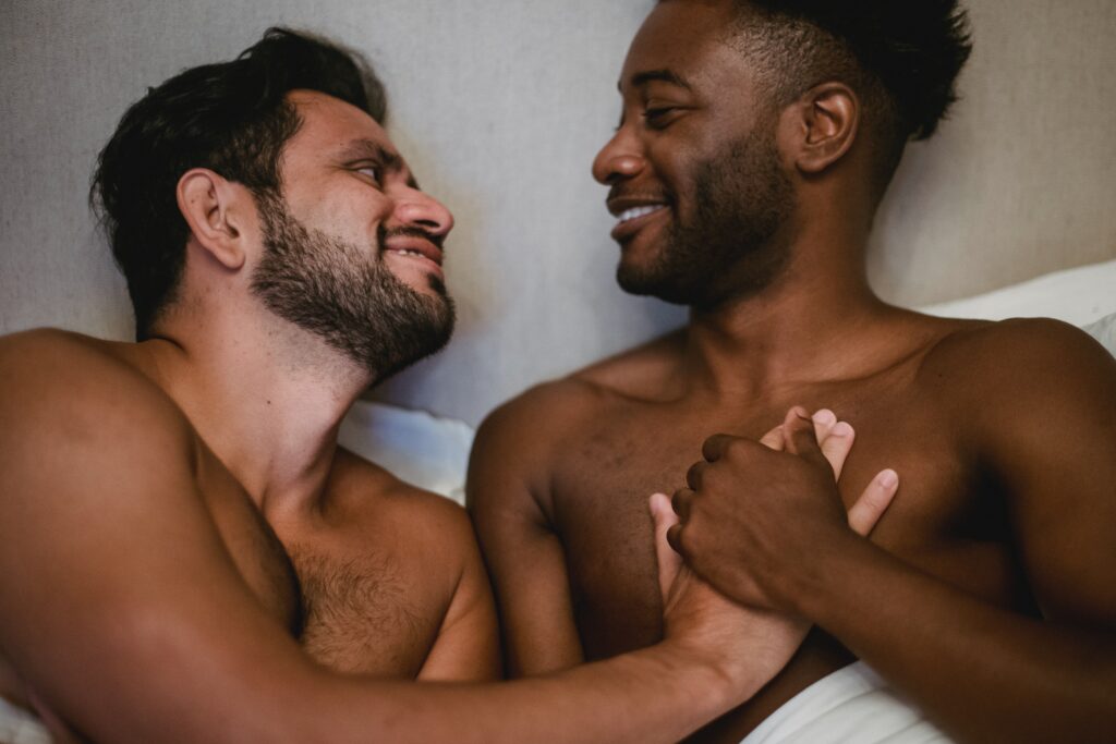 Happy gay couple hold hands in bed