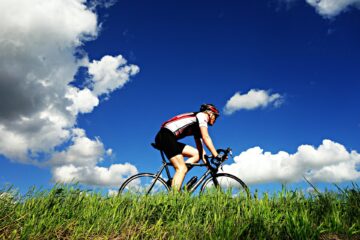 Man rides bike through a a grassy field on a summer day with blue skies