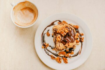 A sweet desert on a plate garnished with walnuts sits beside a partly empty coffee cup