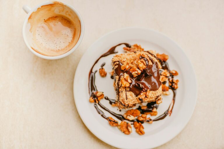 A sweet desert on a plate garnished with walnuts sits beside a partly empty coffee cup