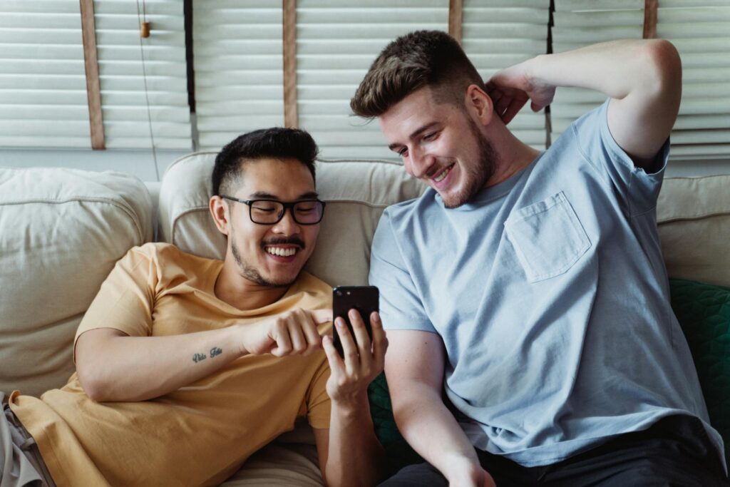 Happy gay couple lounge on a couch making a cellphone call