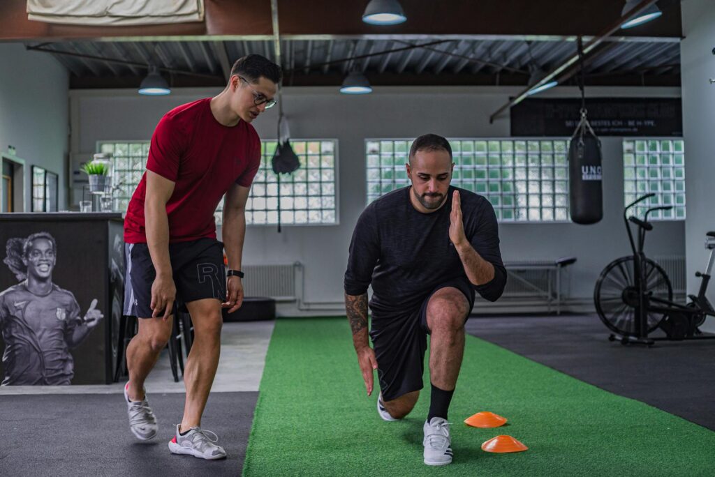 Male personal trainer guides male client through a lunge exercise at the gym.