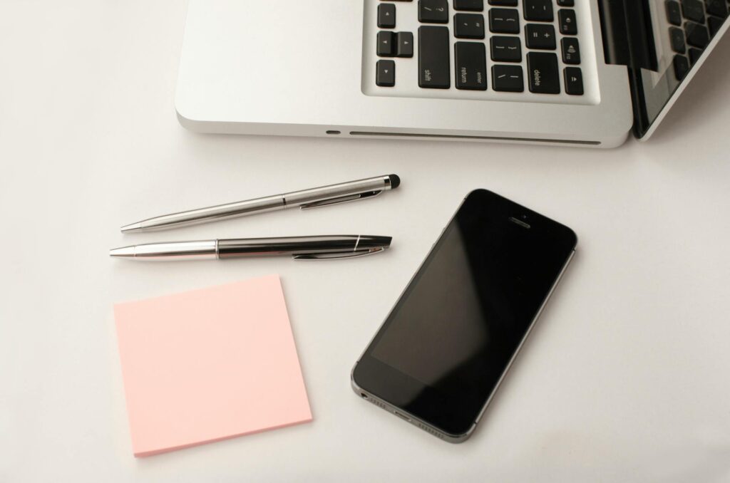Cellphone, laptop, pens, and paper on a desk