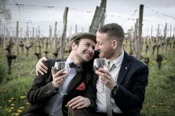 Romantic gay couple enjoy a glass of wine in an orchard