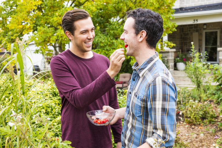 Handsome gay couple in garden sharing cherry tomatos